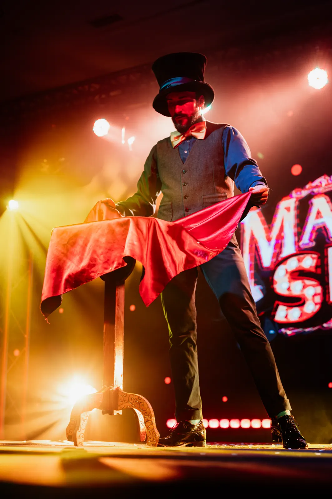 Pan Magiczny w cylindrze odsłania czerwoną chustą iluzję na scenie