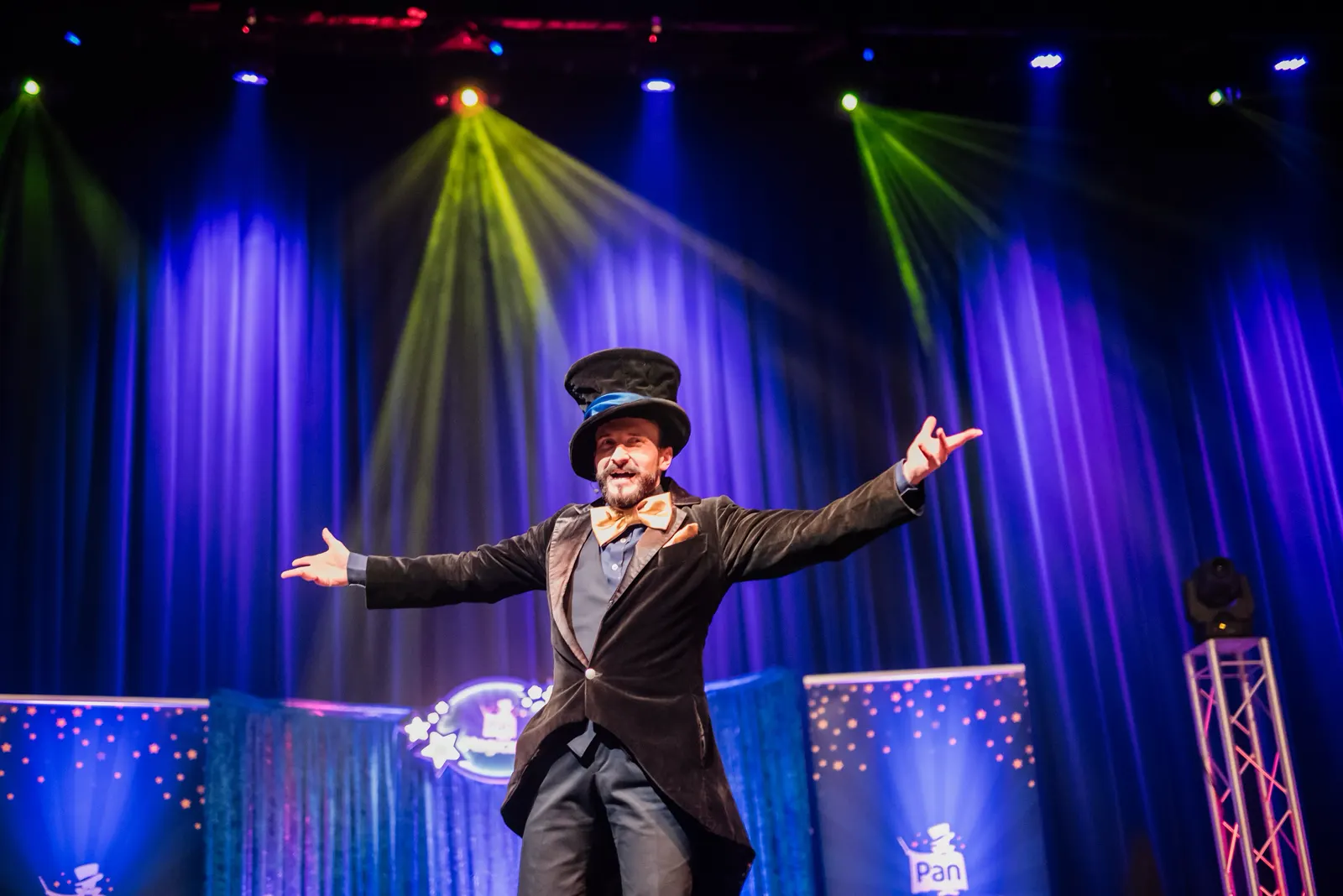 Pan Magiczny w cylindrze z rozłożonymi ramionami na wielkiej scenie teatralnej